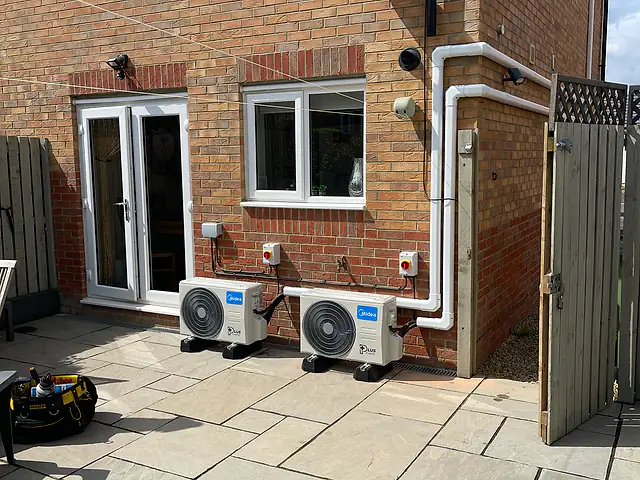 Twin outdoor condensers, London Two outdoor air conditioning units on a patio with white trunking routed neatly along the rear wall of a house